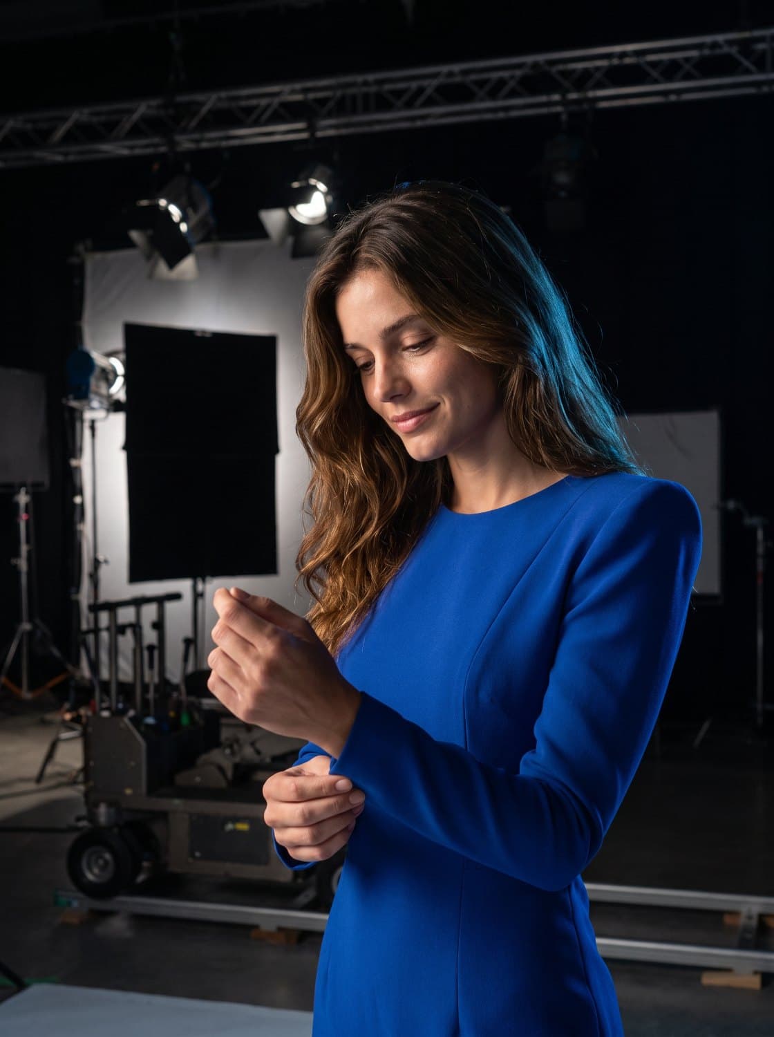 The same character between takes on a film stage, adjusting her cuff under the key light